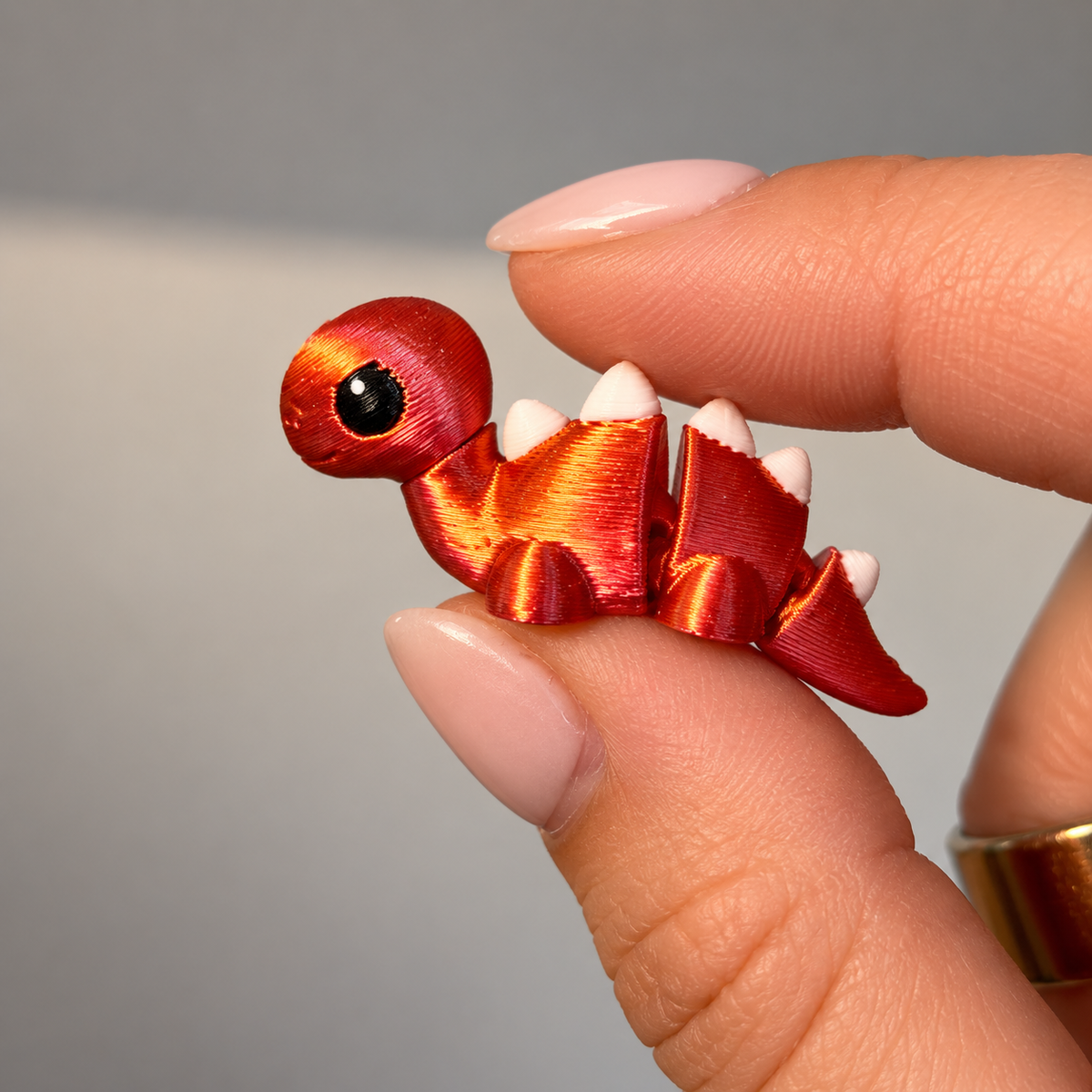 Professional macro photo of the tiny red and white 3D printed mini dino fidget held between fingers