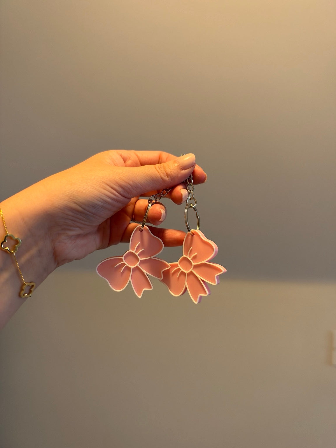 Two pink 3D printed bow keychains held by hand